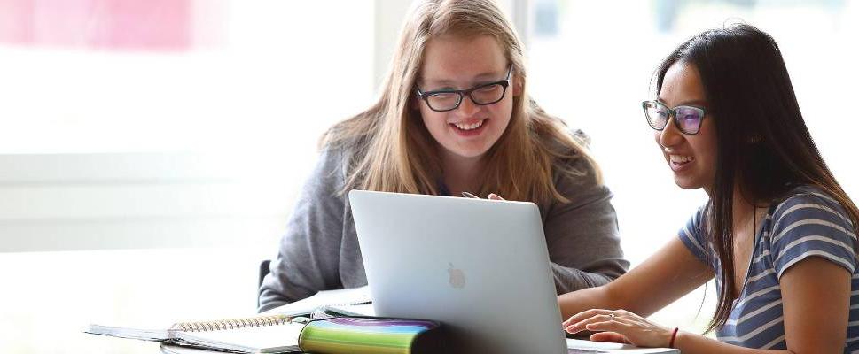 Two students studying with open laptop and stack of books